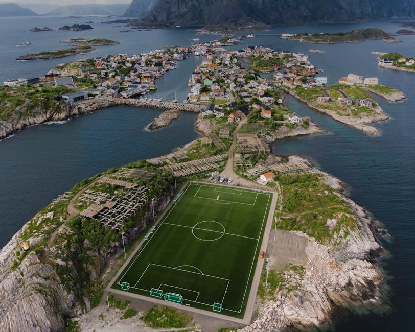 Stunning aerial view of a soccer field on a Norwegian island in Vågan, surrounded by sea and houses.