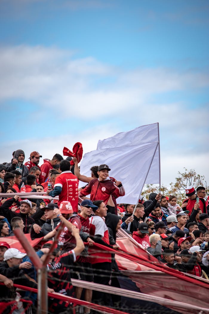 Lively soccer fans dressed in red cheer enthusiastically outdoors, creating a vibrant atmosphere.